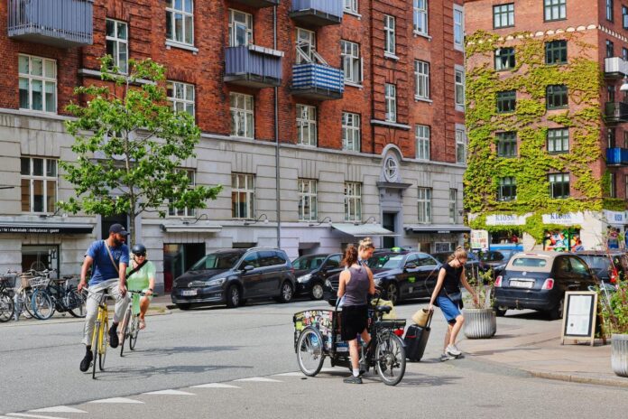 People cycling on a street with brick buildings.